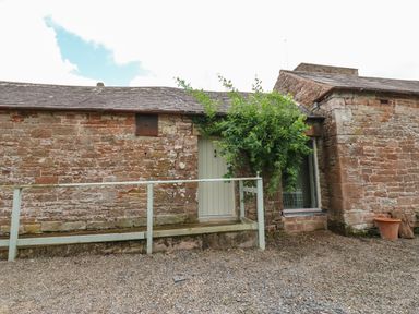 A stone building exterior with a white door and a bush next to a window at The Courtyard in Kirklinton near Longtown