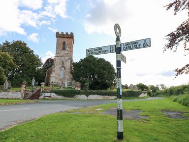 A road junction with a signpost and an old brick church tower with gravestones at The Courtyard in Kirklinton near Longtown