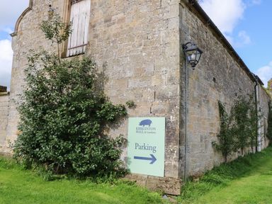 A stone building with a parking sign and bushes at Kirklinton Hall and Gardens