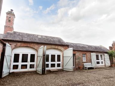 A courtyard with a cobblestone ground and a stone building with white double doors and open shutters at The Courtyard in Kirklinton near Longtown