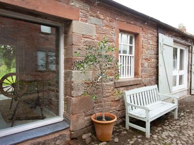 A stone wall with windows a door a potted plant and a white bench at The Courtyard in Kirklinton near Longtown