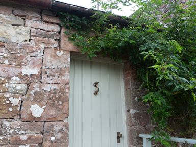 A closed wooden door with a handle surrounded by stone walls and green plants at The Courtyard in Kirklinton near Longtown