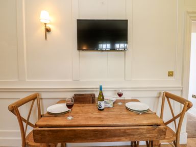 A small wooden dining table set with plates red wine glasses and a wine bottle below a wall mounted television at The Pavillion in Kirklinton near Longtown
