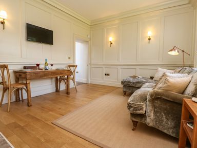 A living room with a wooden dining table, two chairs, a wall-mounted TV, a velvet sofa, and wall sconces at The Pavillion in Kirklinton near Longtown