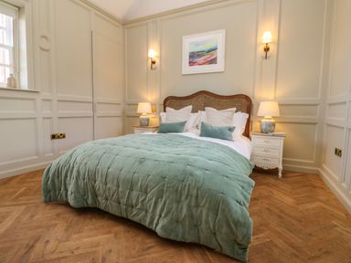 A bedroom with a bed with green bedding two bedside tables with lamps and wall sconces at The Pavillion in Kirklinton near Longtown