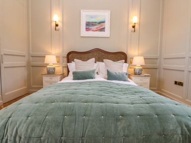 A bedroom with a bed with green bedspread and pillows two bedside tables with lamps and wall sconces at The Pavillion in Kirklinton near Longtown