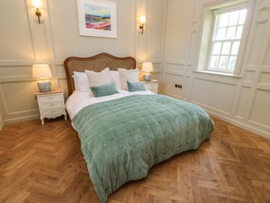 A bedroom with a green quilted bedspread two bedside tables with lamps and a window at The Pavillion in Kirklinton near Longtown
