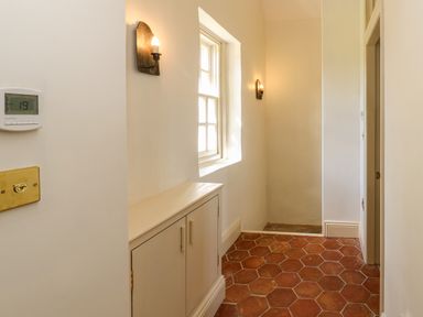 A hallway with terracotta hexagonal floor tiles a window with two wall lights and a cabinet below at The Pavillion in Kirklinton near Longtown