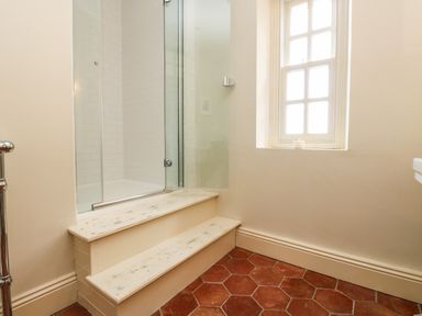 A bathroom with white steps leading to a glass shower enclosure and a window with grid panes at The Pavillion in Kirklinton near Longtown