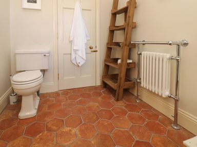 A bathroom with a toilet wooden shelf unit towel on door and a radiator at The Pavillion in Kirklinton near Longtown