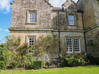 An outdoor seating area with a metal table and two chairs surrounded by rose bushes in front of a stone building at The Pavillion in Kirklinton near Longtown