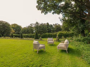 A garden with three chairs on grass surrounded by trees and shrubs at The Pavillion in Kirklinton near Longtown