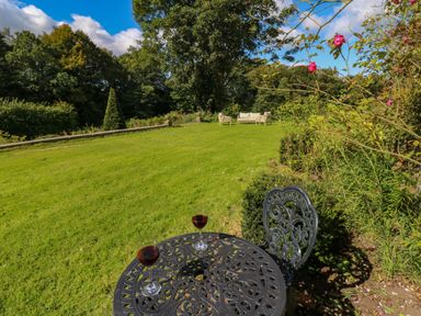 A garden with a metal table and chair with two glasses of red wine on the table and outdoor seating in the distance at The Pavillion in Kirklinton near Longtown