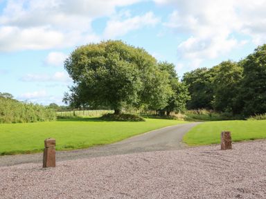 A gravel driveway leading to a paved road with green grass and trees at The Pavillion in Kirklinton near Longtown