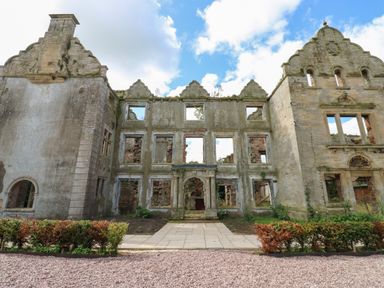 Stone ruins of a building with multiple window openings and an arched entrance surrounded by gravel and low bushes at The Pavillion in Kirklinton near Longtown