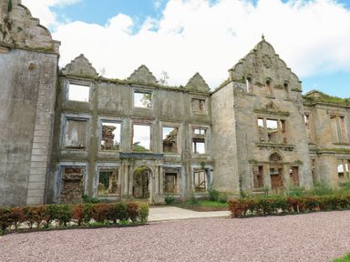 An exterior view of a stone ruin building with empty window frames and overgrown vegetation at The Pavillion in Kirklinton near Longtown