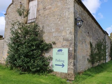 An exterior stone wall with a parking sign and green bushes at Kirklinton Hall and Gardens