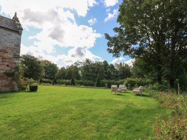 A grassy garden area with outdoor chairs near trees and a stone building at The Pavillion in Kirklinton near Longtown