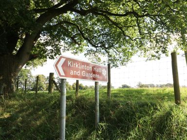 A road sign pointing to Kirklinton Hall and Gardens near a tree and fence in a grassy field at The Pavillion in Kirklinton near Longtown