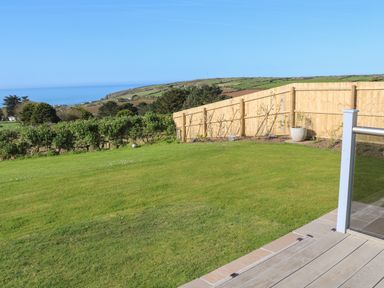 A backyard with grass a wooden fence and a view of the ocean at Greenside Studio in Praa Sands
