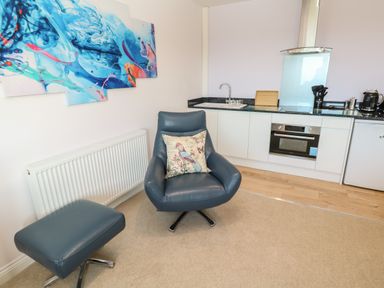 A blue chair with a matching footstool and a pillow in a kitchen area with a sink and oven at Greenside Studio in Praa Sands