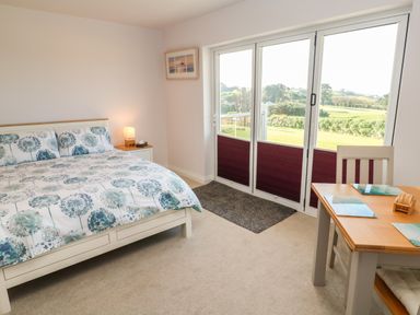 A bedroom with a bed side table a lamp a table with chairs and glass doors leading outside at Greenside Studio in Praa Sands