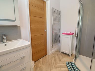 A bathroom with a sink cabinet wooden door towel radiator small white cabinet shower with glass door and striped bath mat at Greenside Studio in Praa Sands
