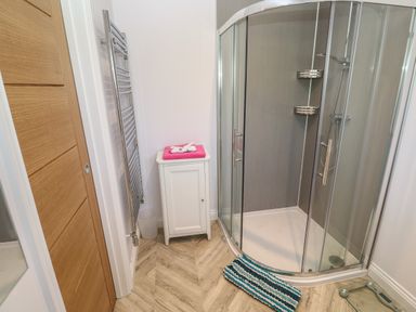 A bathroom with a corner glass shower enclosure a wooden door a white storage cabinet with towels and a towel radiator at Greenside Studio in Praa Sands
