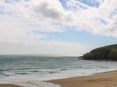 A sandy beach with ocean waves and a rocky hill under a partly cloudy sky at Greenside Studio in Praa Sands