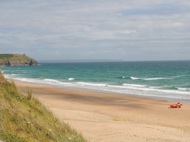 A sandy beach with waves and a red boat on the shore near a grassy cliff at Greenside Studio in Praa Sands