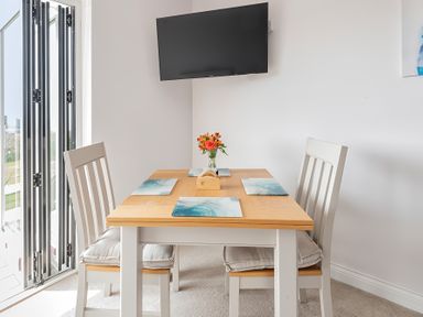 A dining area with a wooden table set for four and a wall-mounted TV at Greenside Studio in Praa Sands