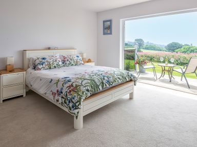 A bedroom with a bed and bedside tables opening onto a patio with chairs and a table at Greenside Studio in Praa Sands