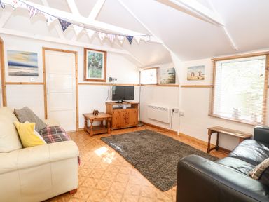 A living room with two sofas a TV on a wooden stand a gray rug and wall art at Suzannes Beach Hut in Bacton near Walcott