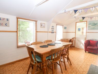 A dining room with a wooden table and six chairs two windows and a red armchair at Suzanne's Beach Hut in Bacton near Walcott