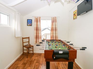 A room with a foosball table wooden chair two framed pictures and a wall-mounted tv at Suzannes Beach Hut in Bacton near Walcott