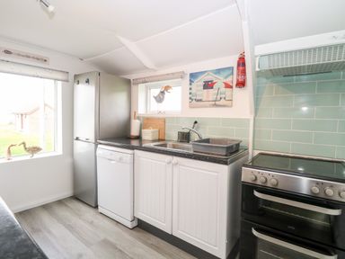 A kitchen with a refrigerator dishwasher sink stove and kitchen utensils at Suzannes Beach Hut in Bacton near Walcott