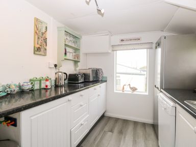 A kitchen with white cabinets black countertop a microwave toaster kettle and decorative items on the window ledge at Suzannes Beach Hut in Bacton near Walcott