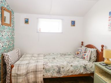 A bedroom with a wooden bed and floral bedding a blanket on a chair and a green nightstand with a yellow lamp at Suzanne's Beach Hut in Bacton near Walcott