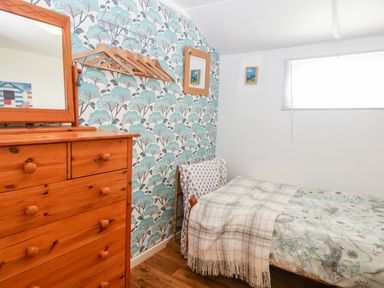 A small bedroom with a wooden dresser a bed with patterned bedding and floral wallpaper at Suzanne's Beach Hut in Bacton near Walcott