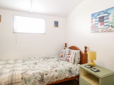 A bedroom with a single bed wooden headboard floral bedding two pillows green bedside table with yellow lamp and a window at Suzanne's Beach Hut in Bacton near Walcott