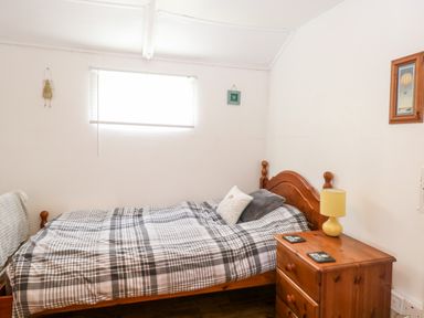 A bedroom with a single bed a wooden bedside table and a window at Suzanne's Beach Hut in Bacton near Walcott