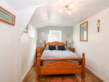 A bedroom with a wooden double bed two bedside tables with lamps a mirror on the wall and wooden flooring at Suzanne's Beach Hut in Bacton near Walcott