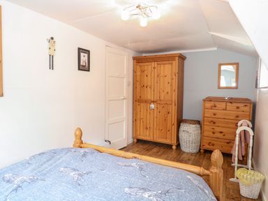 A bedroom with a wooden bed a wooden wardrobe a wooden chest of drawers and a towel rail at Suzannes Beach Hut in Bacton near Walcott