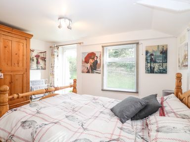 A bedroom with a wooden bed a wooden wardrobe paintings on the walls and a window with blinds at Suzannes Beach Hut in Bacton near Walcott