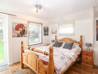 A bedroom with a wooden bed and bedside tables next to windows with blinds at Suzanne's Beach Hut in Bacton near Walcott