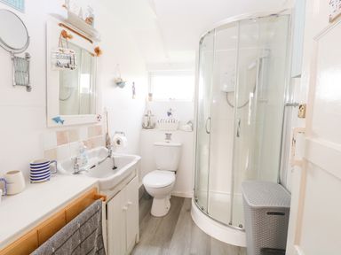 A bathroom with a sink a toilet a curved glass shower and a laundry basket at Suzannes Beach Hut in Bacton near Walcott