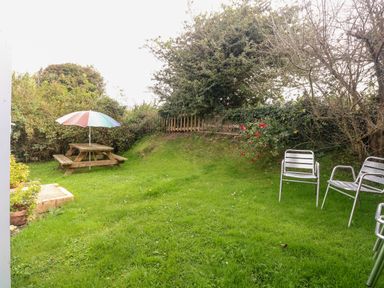 A garden with a wooden picnic table and umbrella metal chairs and green grass at Suzannes Beach Hut in Bacton near Walcott