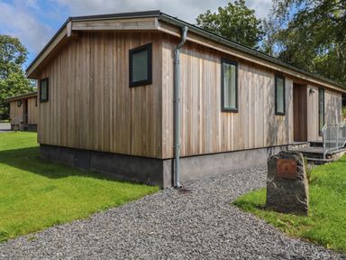 A wooden building with several windows and a gravel path leading to the entrance at The Beeches in Haverthwaite