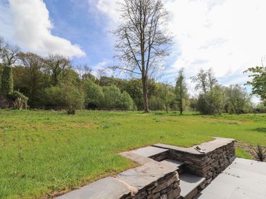 A grassy backyard with stone steps leading to a lawn and trees in the background at The Yews in Haverthwaite