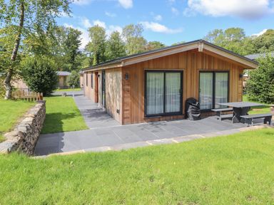 A wooden cabin with sliding glass doors and outdoor seating on a tiled patio at Millstream Ridge in Haverthwaite